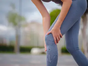 Woman grabs hurt knee during morning run.